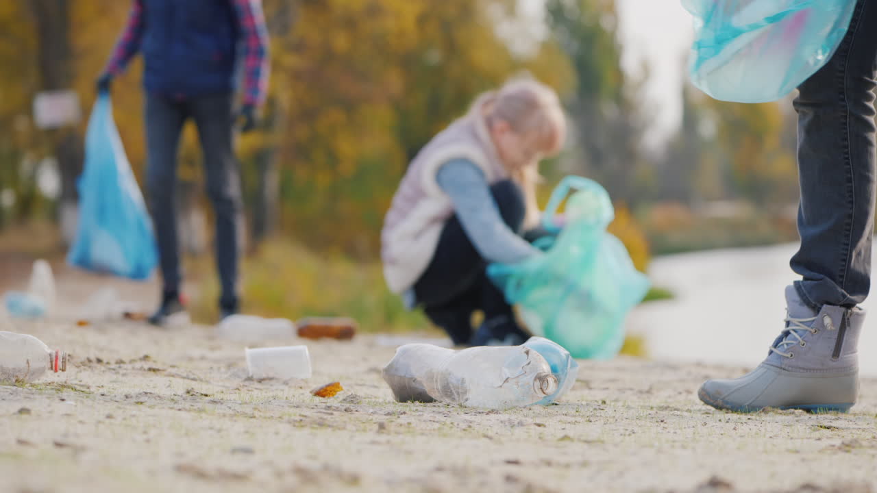 자원 봉사자 그룹이 호수 더미에서 쓰레기를 줍고 플라스틱 쓰레기를 가방에 담습니다.