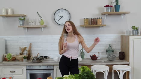 encantadora chica vegana con cabello largo bailando y cantando en la cocina moderna. dieta de alimentos vegetales crudos