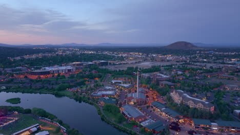 aerial drone view of the old mill district in bend oregon. drone flying backwards over deschutes river at night. pilot butte in the distance.