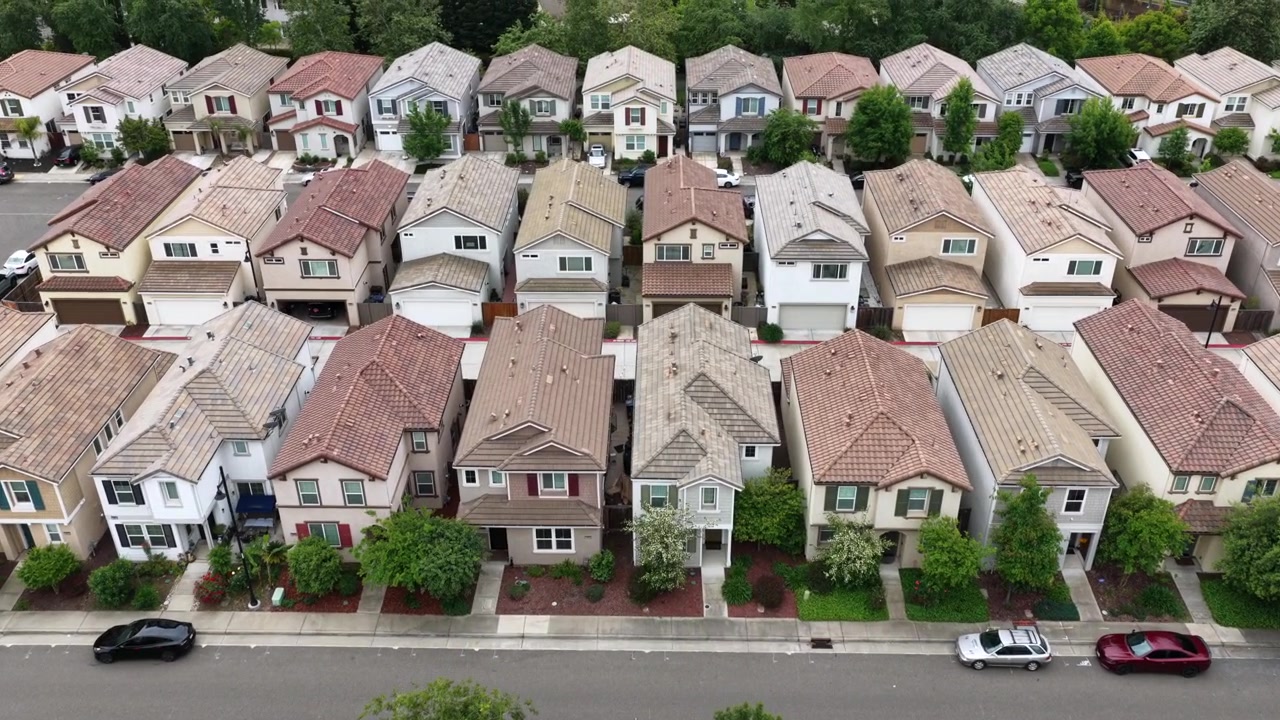 Rancho Cordova, file fitte di case a schiera a due piani con tetti in terracotta e garage annessi che riempiono l'inquadratura da un lato all'altro, auto parcheggiate sulla strada sottostante. California, USA. Ripresa aerea in sorvolo.