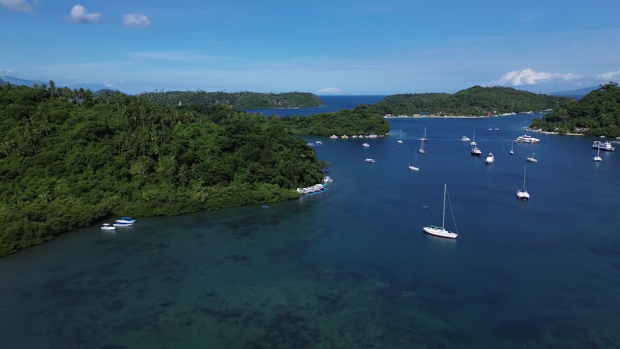 Filmato aereo realizzato con drone di piccole imbarcazioni ancorate in una tranquilla baia tropicale a Puerto Galera, nelle Filippine, circondata da una fitta foresta verde e da acque cristalline turchesi, che creano una scena di viaggio e natura rilassante