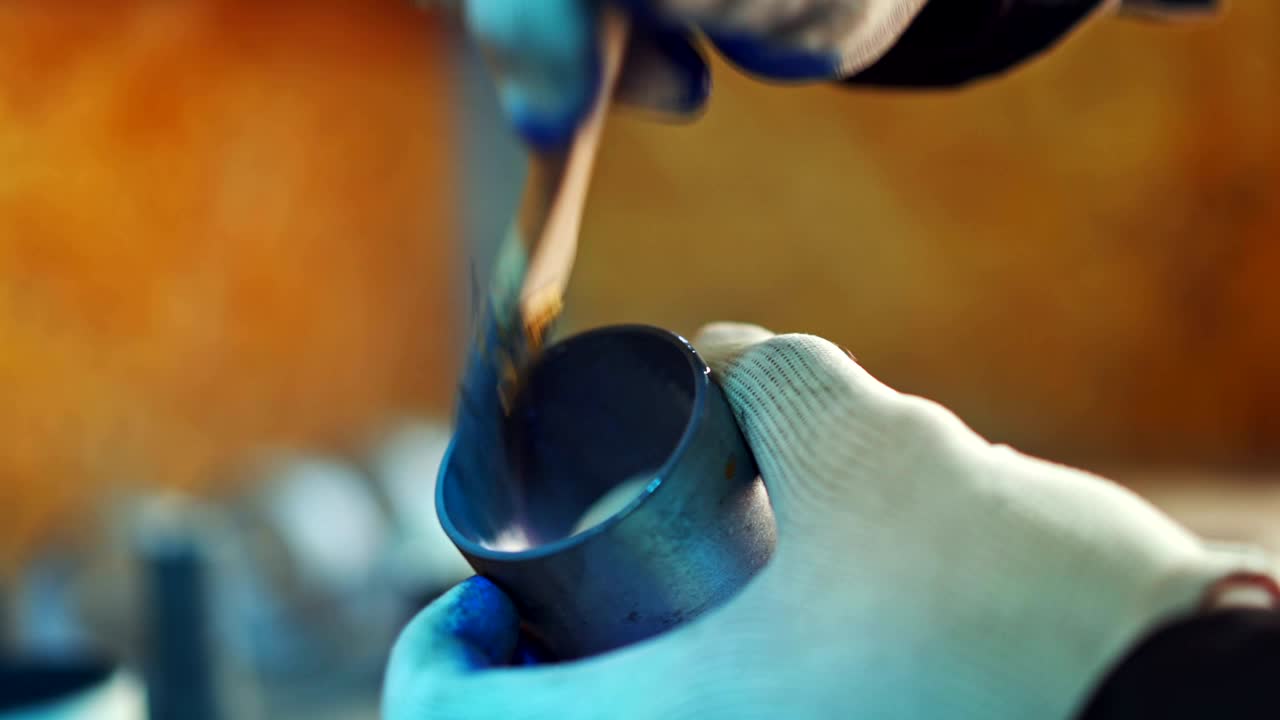 un trabajador sostiene un rodamiento de bola en la mano y lo colorea con pincel de color azul sobre un fondo borroso.