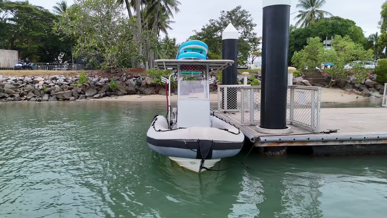 An inflatable boat approaches and docks at a marina in Port Douglas, surrounded by lush greenery and calm waters