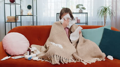 sick ill girl child suffering from cold flu allergy infection wrapped in blanket sits on home sofa