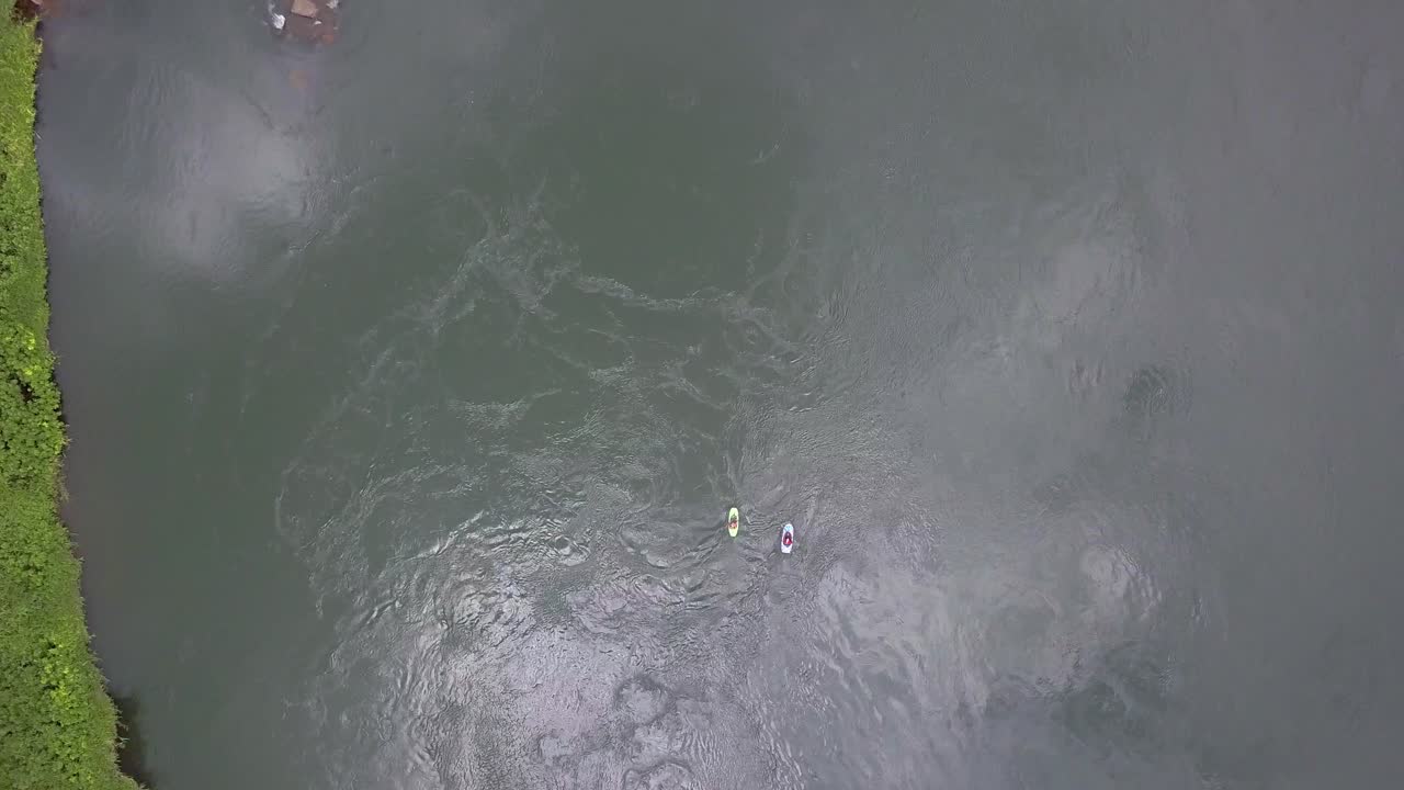 Top down aerial drone view showing two kayaks on the River Nile in Jinja, Uganda, moving over calm, deep green water with visible surface ripples and reflections under soft tropical daylight