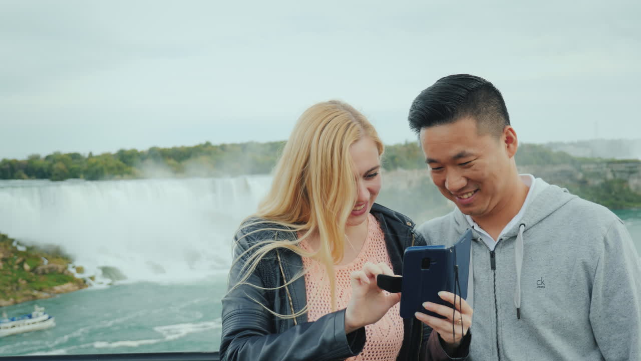 un joven asiático y su novia caucásica están mirando una foto en un teléfono en el observati