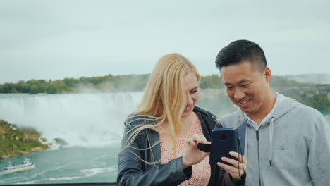 a young asian guy and his caucasian girlfriend are looking at a photo on a telphone on the observati