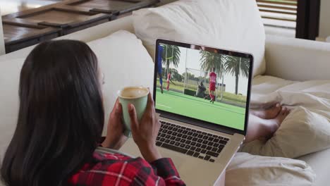 Compuesto-De-Mujer-Sentada-En-Casa-Sosteniendo-Un-Café-Viendo-Un-Partido-De-Hockey-En-Una-Computadora-Portátil