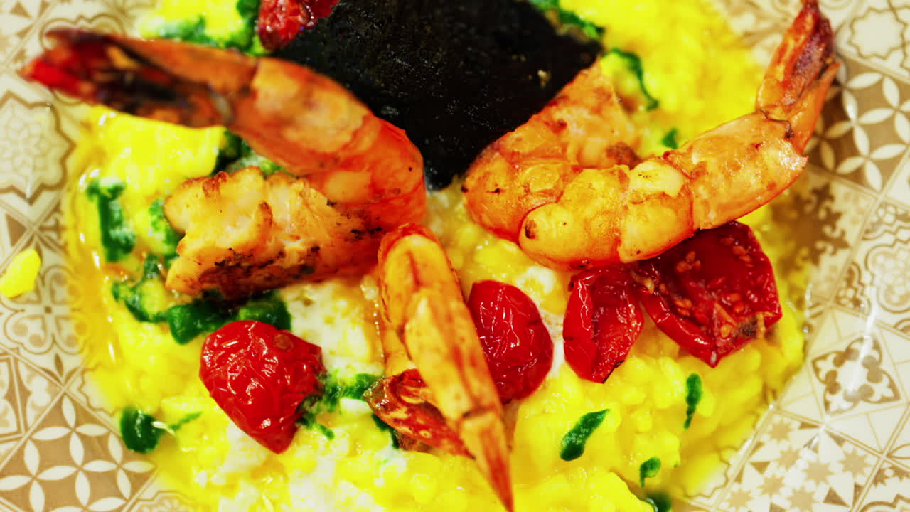 Close up of saffron risotto topped with grilled prawns and roasted cherry tomatoes
