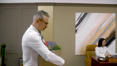 hombre elegante con camisa blanca y corbata gris saliendo de la oficina con sus cosas personales en una caja