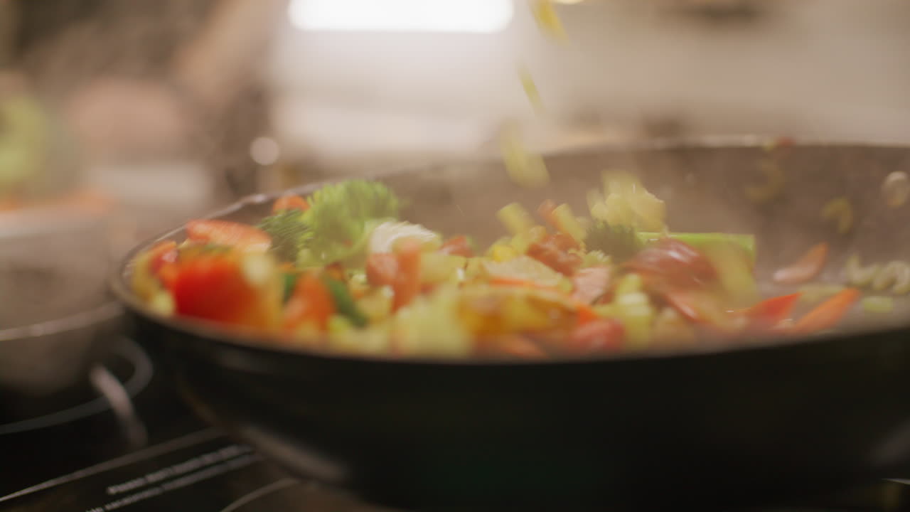 Primo piano di un cuoco che salta verdure in una padella calda durante la cottura.