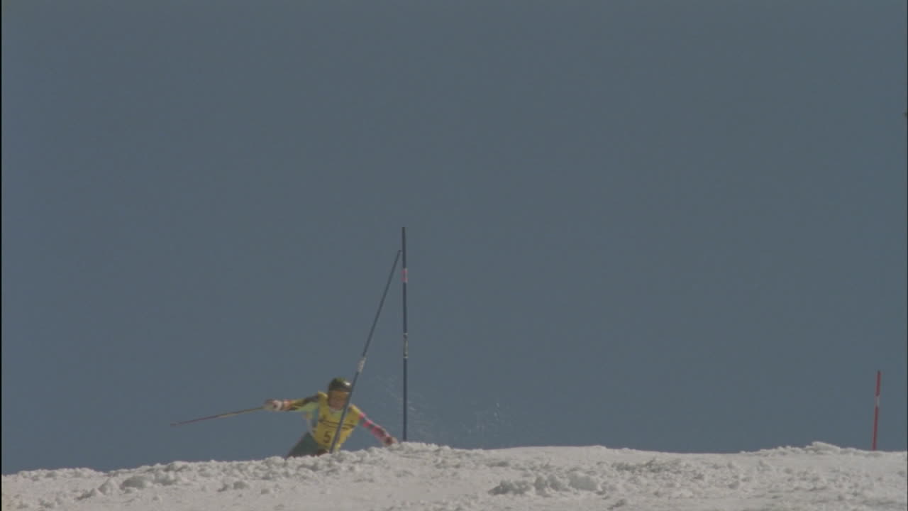 한 스키어가 폴 주위를 스키를 타고 슬로프를 계속 내려갑니다.