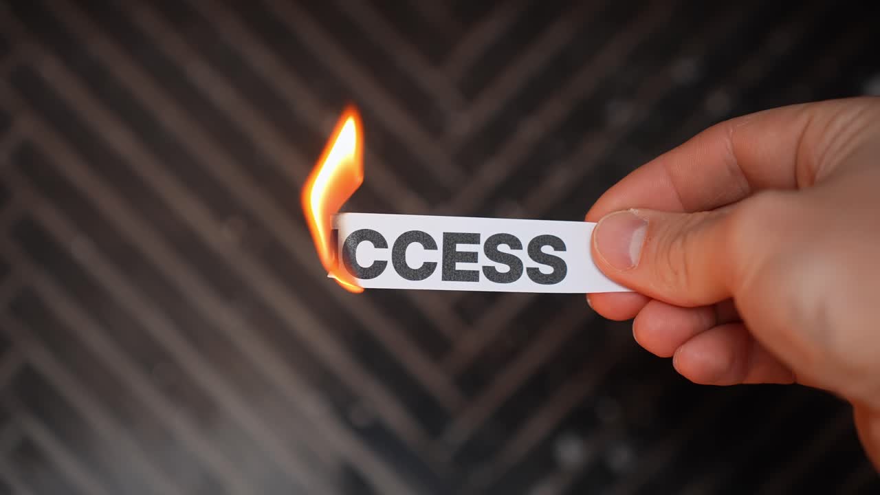 Hand burns a paper label reading “SUCCESS,” symbolizing failure, lost dreams, broken goals, and burnout. Dark background with copy space for crisis or depression concept