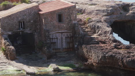 Turquoise-waters-set-before-a-boat-shed-in-Mallorca,-Spain,-creating-a-tranquil-scene-of-coastal-charm