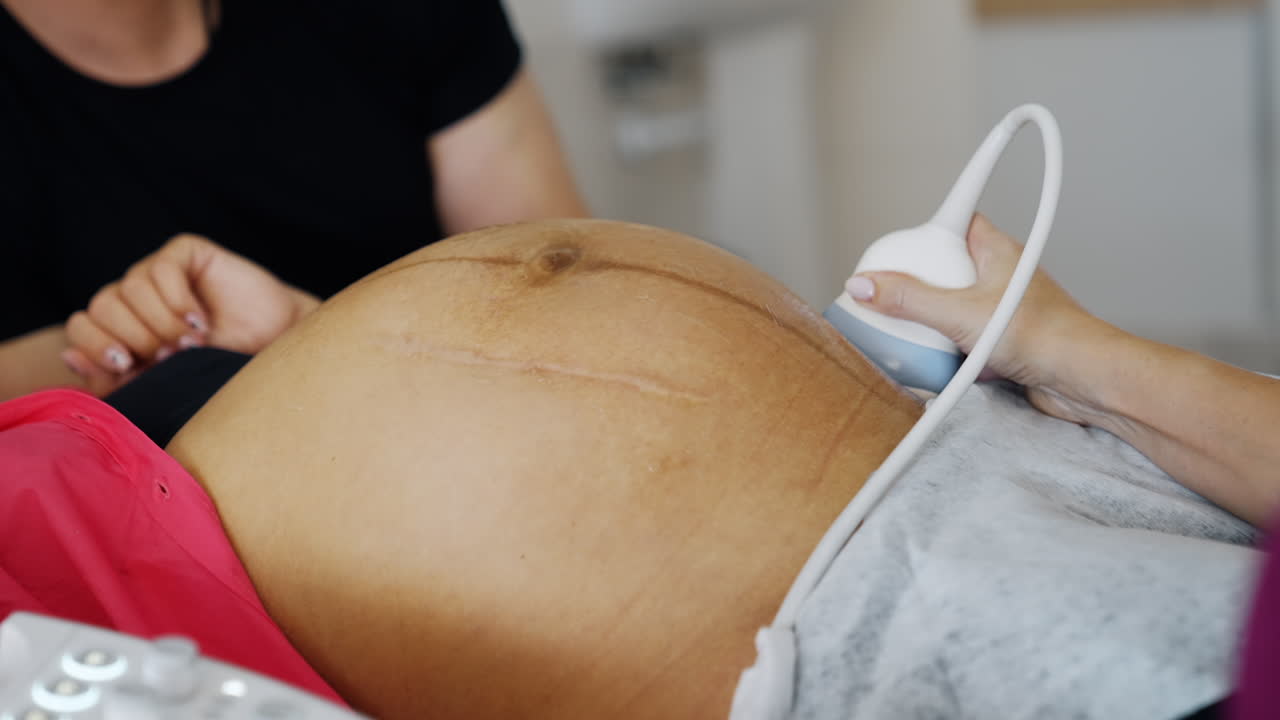 Doctor's hand moving ultrasound transducer by the big pregnant belly of an unrecognized woman. Checking the pregnancy on the last stages before baby delivery.