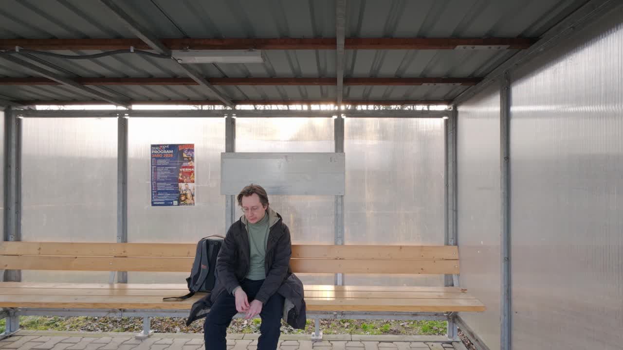 Un uomo in viaggio da qualche parte guarda un poster alla fermata dell'autobus. Si siede su una panchina e controlla l'ora