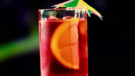 a close-up of a red cocktail with ice, orange slice, and a decorative umbrella against a dark background.