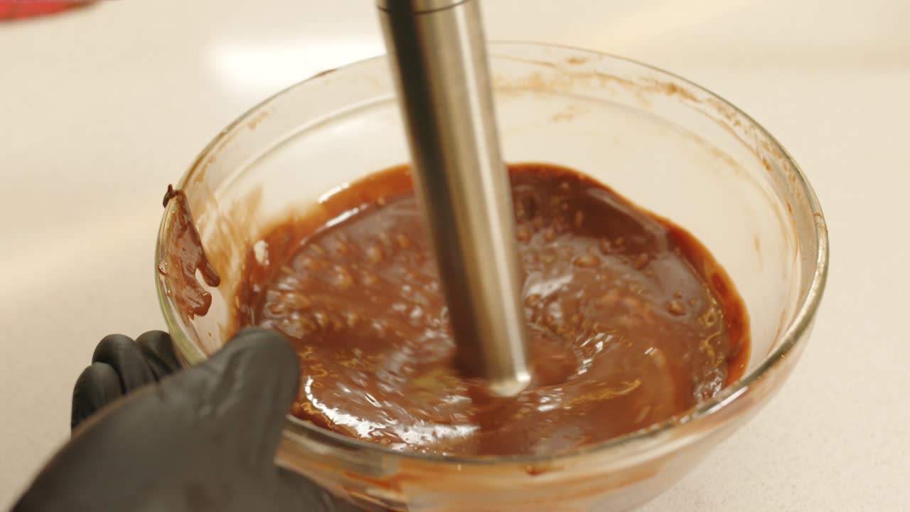 Close up gimbal shot of hands with mixer mixing chocolate