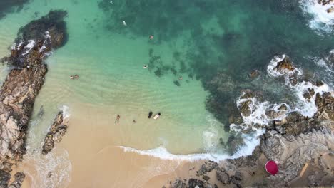 Jib-down-and-tilt-up-above-small-beach-with-people-in-a-sunny-day