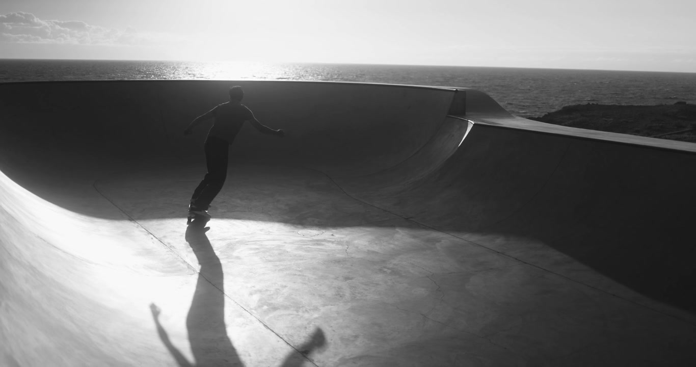 Silhuet af en skateboarder, der kører i en skatepark ved havet