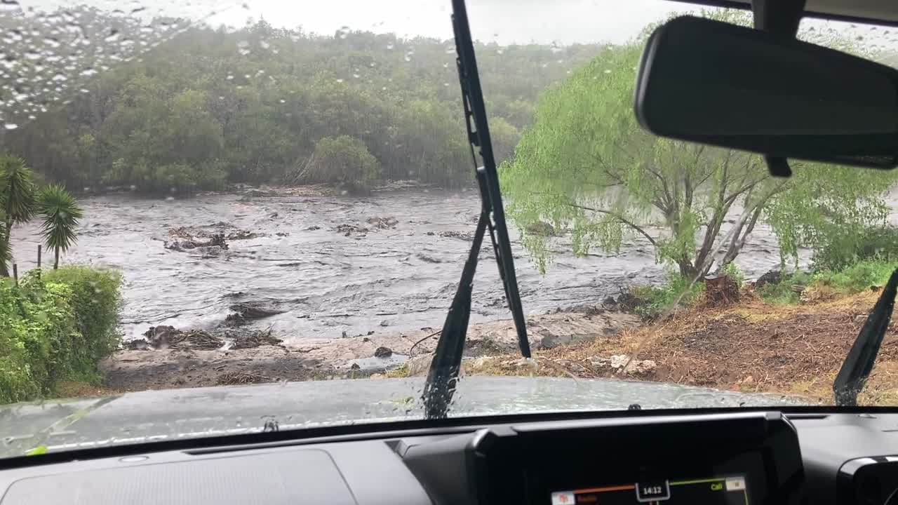 Una vista attraverso il parabrezza di un'auto sotto la pioggia su un fiume in piena.