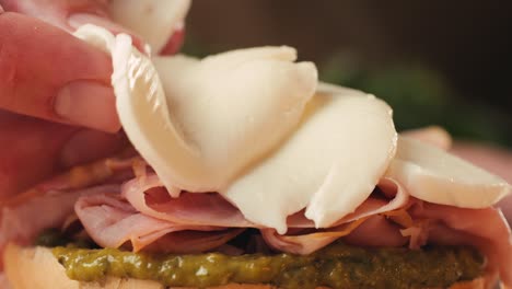 mortadella ham sandwich, traditional italian focaccia filled with thin pesto slices of mortadella, served by chef man in cafe restaurant. macro of traditional italian spanish tapas antipasti.