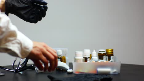 doctor putting on black gloves to start patient examination with stethoscope and electronic thermometer with pills on the table