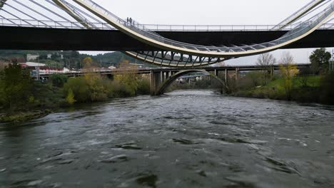 Drone-Vuela-Debajo-Del-Puente-Del-Milenio-Río-Miño-En-Ourense,-Galicia,-España-Retrocediendo