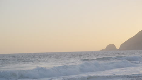 slow motion panning shot of waves rolling in along mondo's beach as the sun sets behind a mountain at golden hour located in southern california