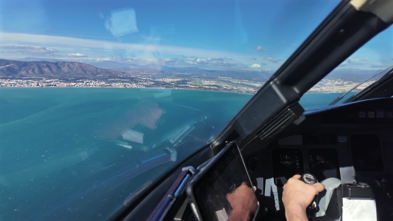 Mano di un pilota caucasico che prende il controllo manuale di un jet afferrando la barra di comando, mentre sorvola il mare con la pista dell'aeroporto di Malaga (AGP) di fronte, in una giornata soleggiata e ventosa