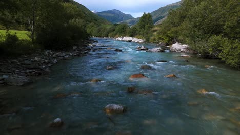 Drone-flying-slow-over-Furka-pass-river-water-stream-surface-in-summer-season,-Switzerland