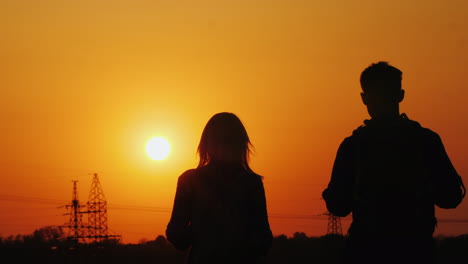 Zwei-Reisende-Mit-Rucksäcken-Gehen-Vorwärts-In-Richtung-Der-Untergehenden-Sonne-Und-Der-Stadt-Aktives-Leben