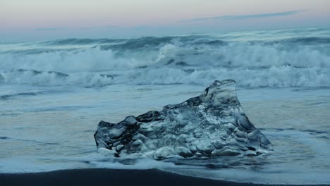 located on the black diamond beach in iceland, iceblock is washed up by the ocean during sunset