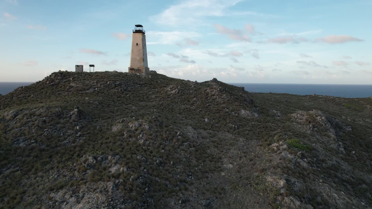una vista panorámica aérea inclinada sobre una ladera rocosa, revelando un faro lejano y la belleza natural de gran roque en el archipiélago de los rocas, venezuela