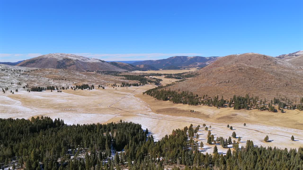 Drone flight revealing the scale of the Jemez Mountains and Valles Caldera. The shot highlights the contrast between the green pine forest and the open volcanic valley floor in winter