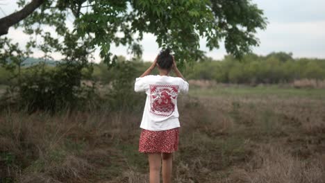 A-woman-in-a-white-shirt-and-red-skirt-walks-through-a-grassy-field-on-a-cloudy-day