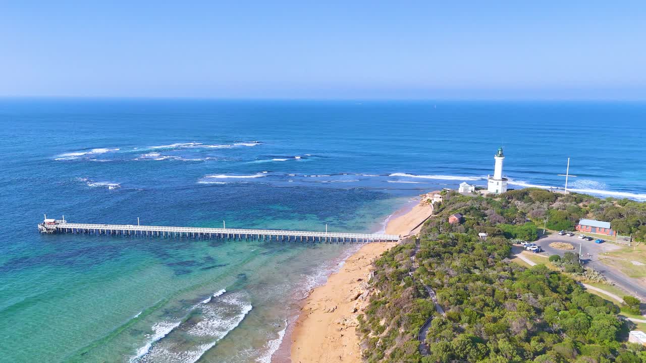 Aerial footage captures Point Lonsdale's lighthouse, pier, and coastline under clear skies, showcasing vibrant ocean hues and lush greenery