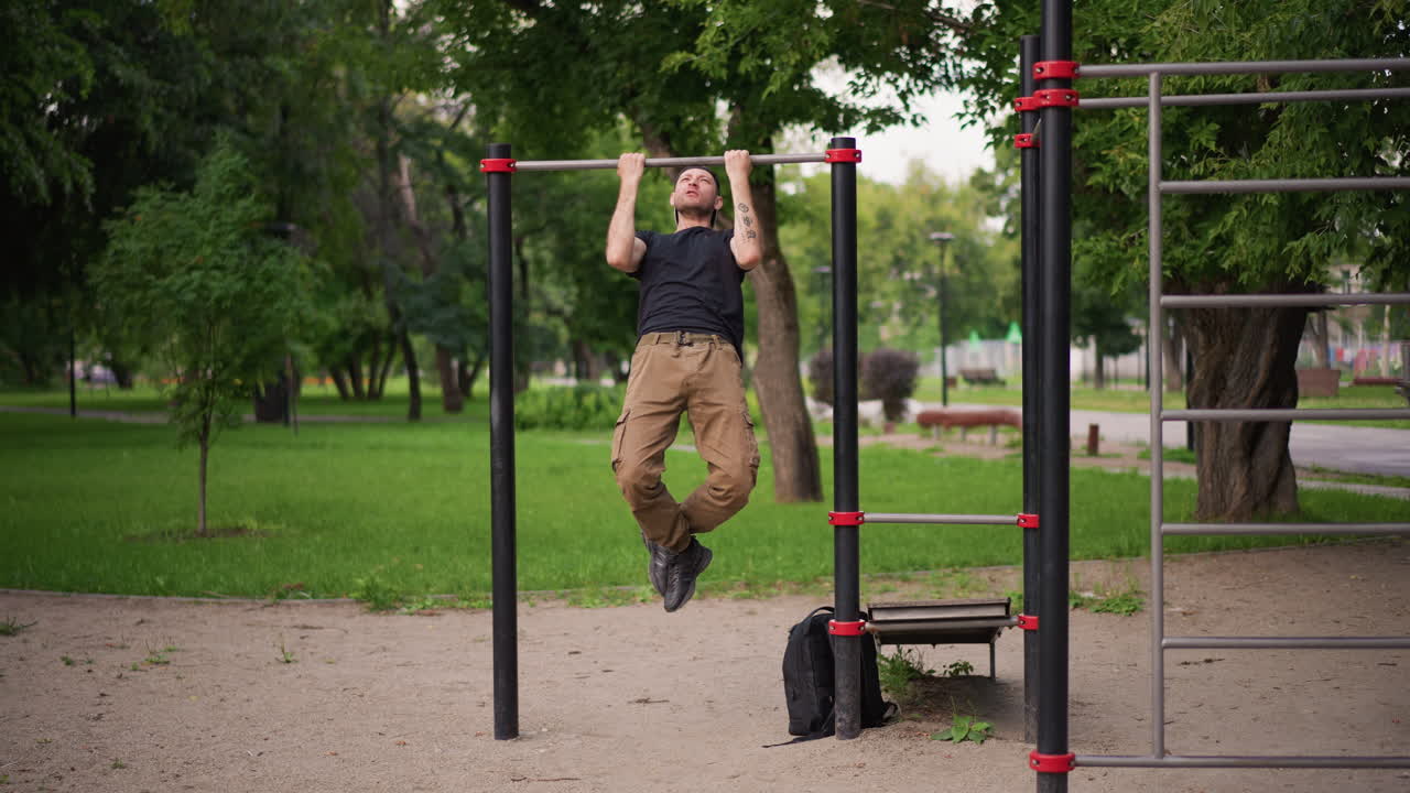 Athlete Attempts Chinup, Jumping Athlete Reaches For Pullup Bar Outdoors, Person In City Park Aims For Chinup On Bar, Fitness Enthusiast Jumps For Pullup Inside City Park With Green Scenery