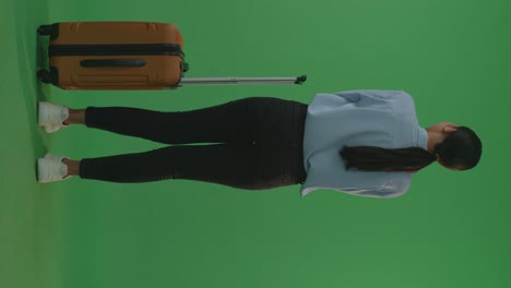 full body of back view asian woman traveler with luggage crossing arms and looking around while standing in the green screen background studio, during sunset time