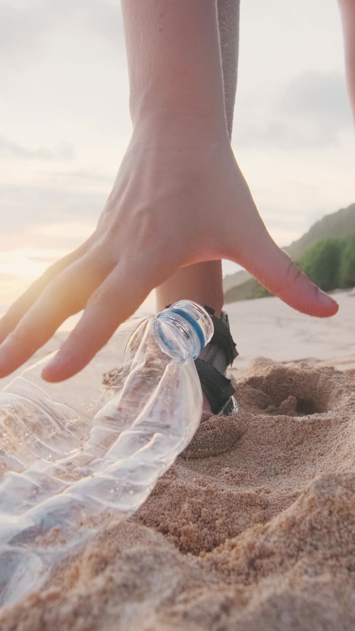 Close up hands of volunteer removing plastic trash and bottles from sandy beach