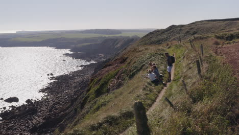 Drone-Shot-Of-Group-Of-Friends-Hiking-Along-Cliffs-On-Coastal-Path