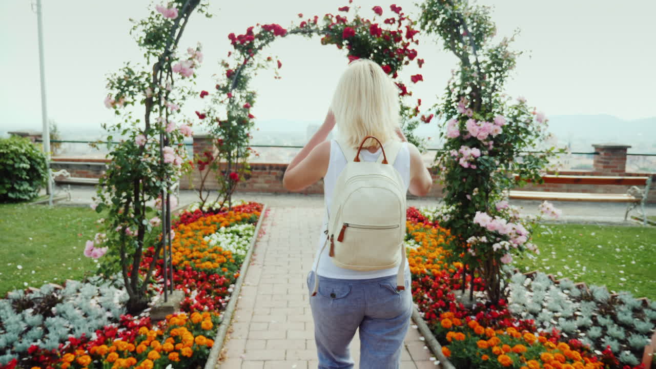 vista posterior: una mujer joven está caminando en el jardín de rosas