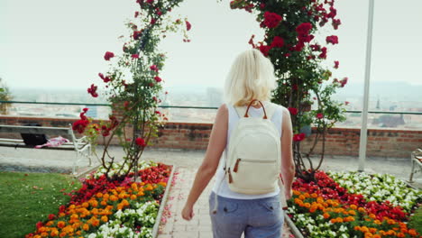 back view: a young woman is walking in the garden of roses