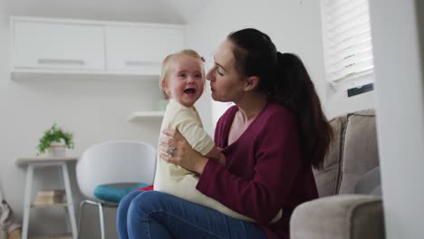 Kaukasische-Mutter-Spielt-Mit-Ihrem-Baby-Und-Küsst-Es,-Während-Sie-Zu-Hause-Auf-Der-Couch-Sitzt