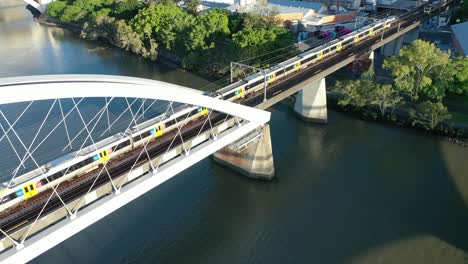 trains crossing river on brisbane's iconic merivale railway bridge, suspended over the beautiful brisbane river, west end, south bank, and brisbane city visible in this stunning drone shot