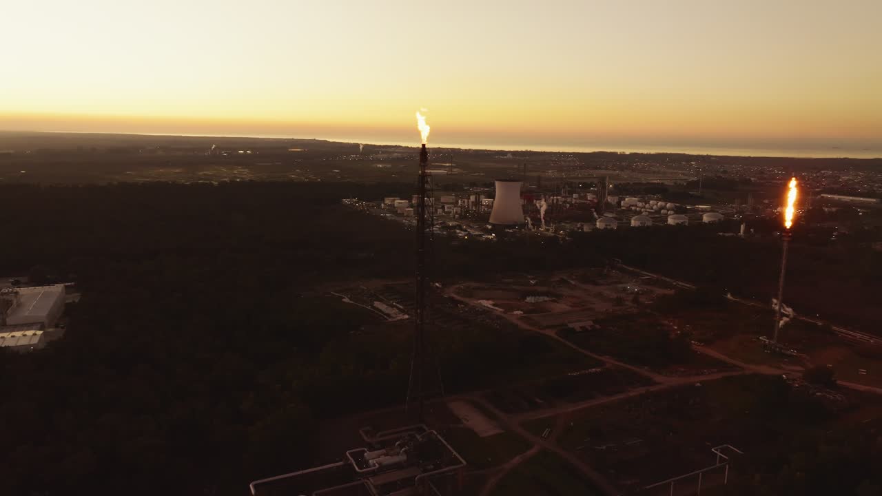 Drone aerial view of an active oil refinery, showing chimneys emitting flames and smoke while the plant is in operation