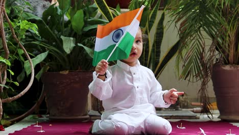 Niedliches-Kleinkind-Schwenkt-Indische-Trikolore-Flagge-In-Traditionellem-Stoff-Mit-Unschuldigem-Gesichtsausdruck