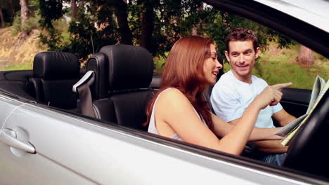 una pareja perdida mirando un mapa de la carretera en un coche convertible