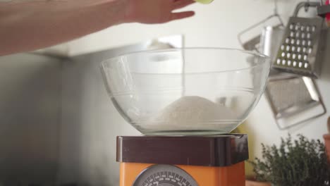 static shot of a person putting ingredients in a bowl on a vintage cooking weight scale