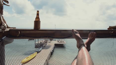 pov point of view of a man laying down on a hammock taking the sun and tanning while he relaxes and drinks a beer on a beach in hotel ecohouse isla fuerte colombia